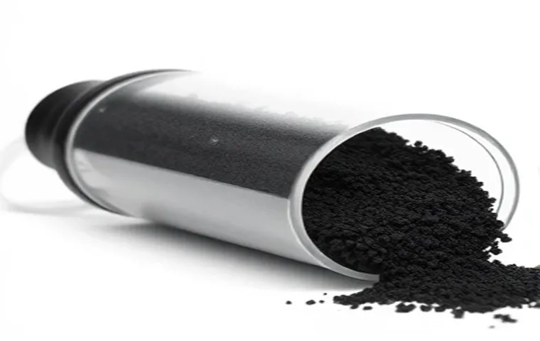 یک محفظه استوانهای شفاف و افقی فیلتر پست کربن که حاوی گرانولهای سیاه کربن فعال است و بخشی از آن بر روی یک سطح سفید ریخته شده است